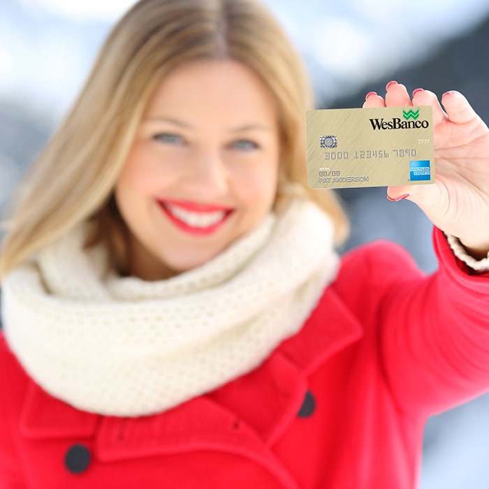 Smiling blonde woman in a red winter coat with white trim excitedly holds up a Personal WesBanco Credit Card