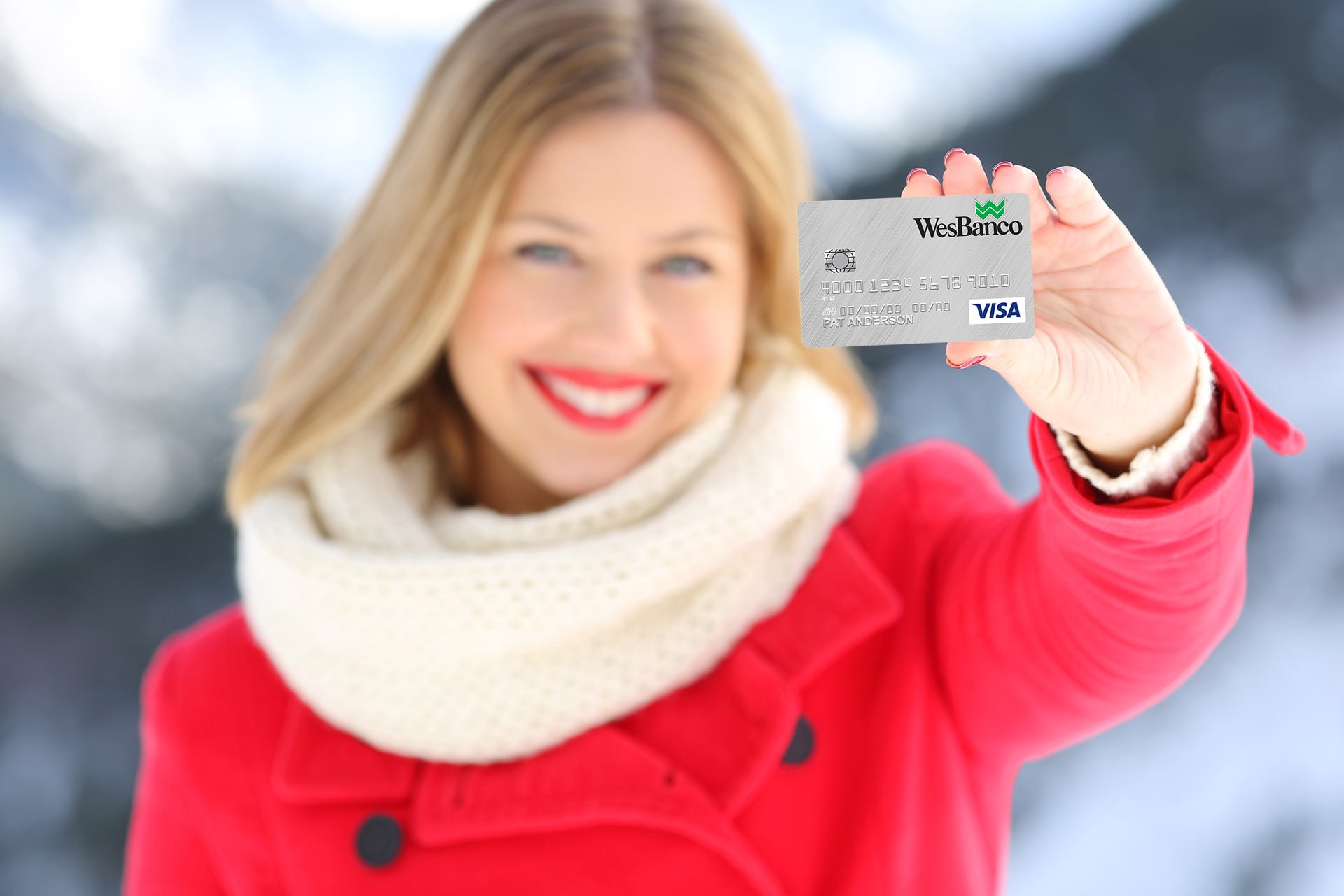 Smiling blonde woman in a red winter coat with white trim excitedly holds up a Personal WesBanco Credit Card