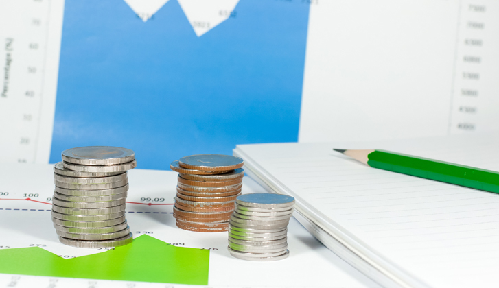 A stack of coins sit in front of a financial chart in blue.