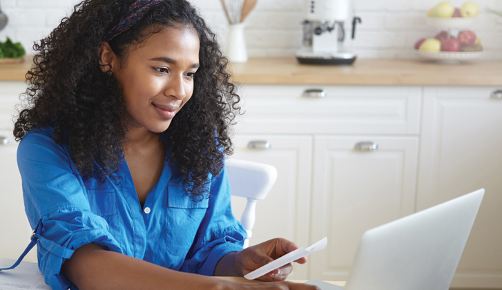 Young woman at dining table with fond smile inputs information into her computer.