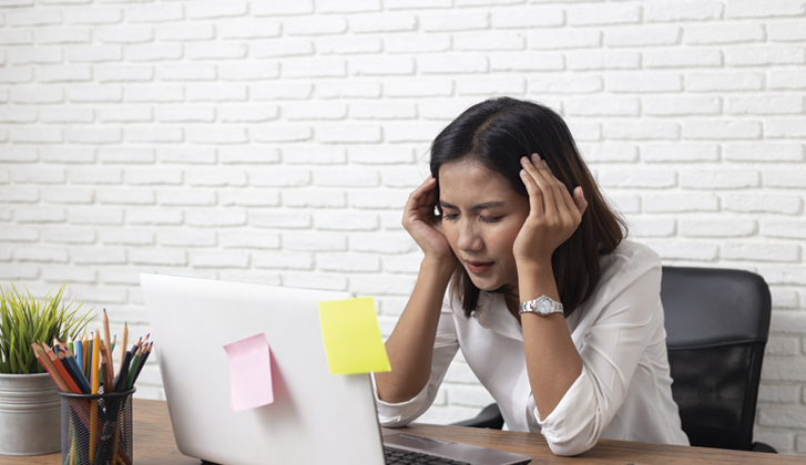 Female office worker holds her head with eyes closed due to stress.