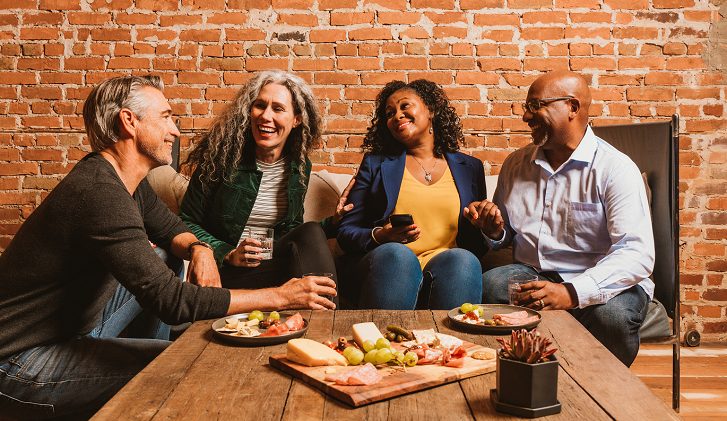 group of four sitting at a table with a cheeseboard and their phones out