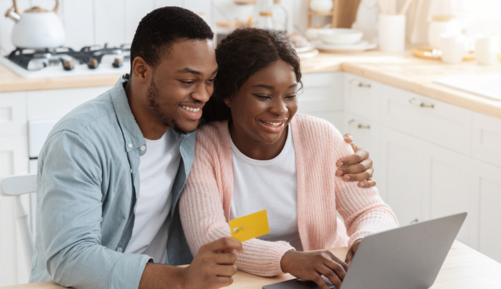 Af.Am. couple hugging, smiling and looking at a computer together.