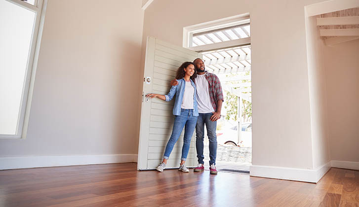 Couple Opening Door And Walking In Empty Lounge Of New Home