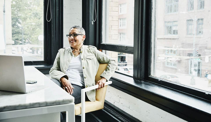 Business woman sitting at an office desk in casual clothing smiling at the computer screen